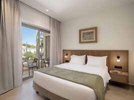 Una habitación de hotel con una cama grande, una mesita de noche, una lámpara de pared y una ventana con cortinas.