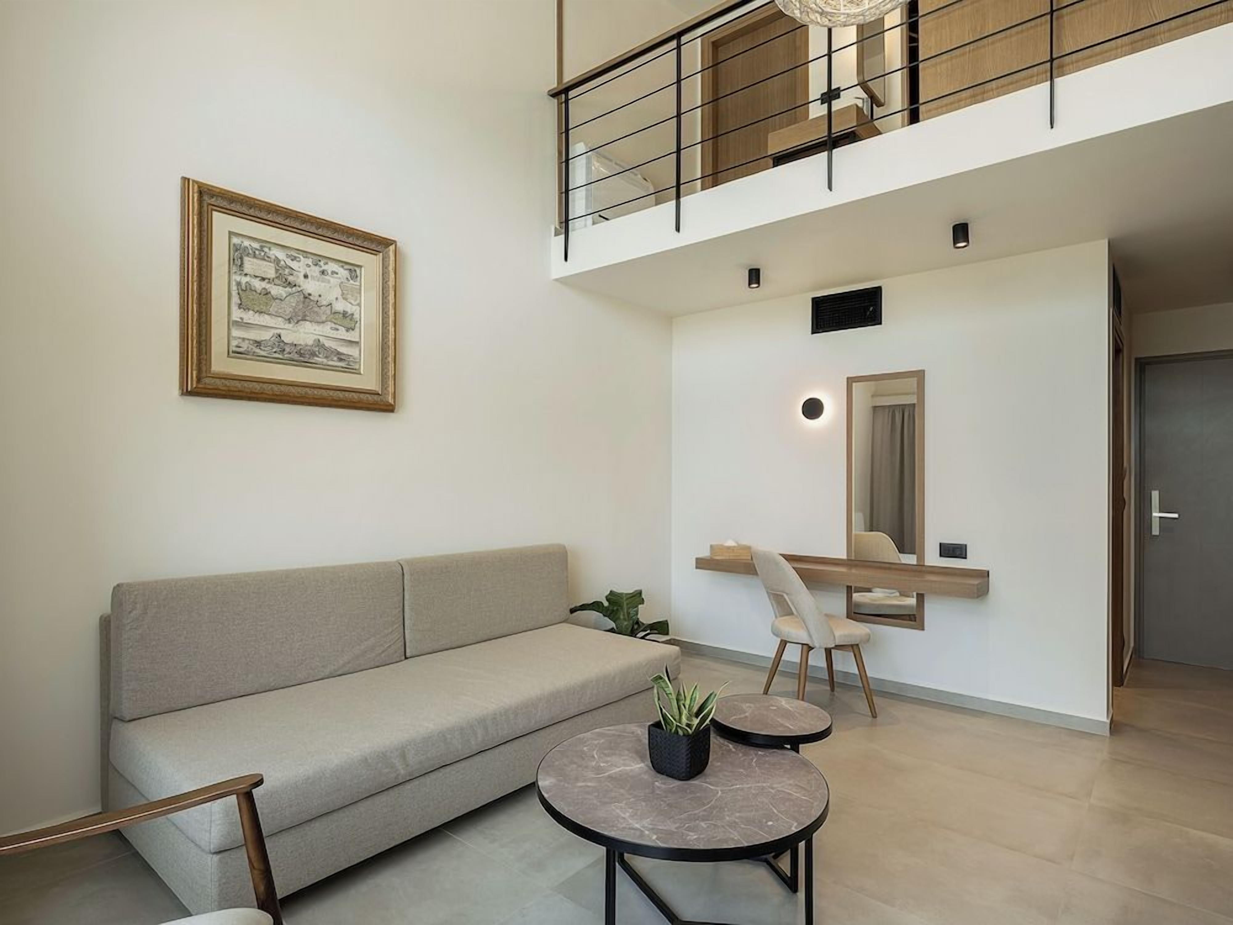 A modern living room with a sofa, two round tables, a framed picture, a mirror, and a staircase.