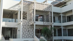 Un edificio de varios pisos con diseño moderno, que presenta una fachada geométrica, un área de estar al aire libre y una escalera que conduce a la entrada.