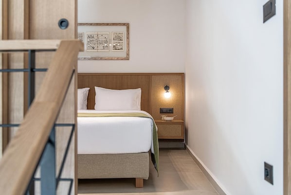 Una habitación de hotel con una cama, una mesita de noche, una lámpara de pared e imagen enmarcada sobre la cama.