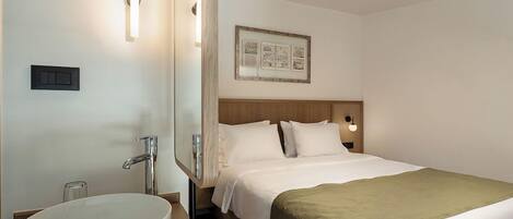 A hotel room with a bed, a round sink, and a framed picture on the wall.