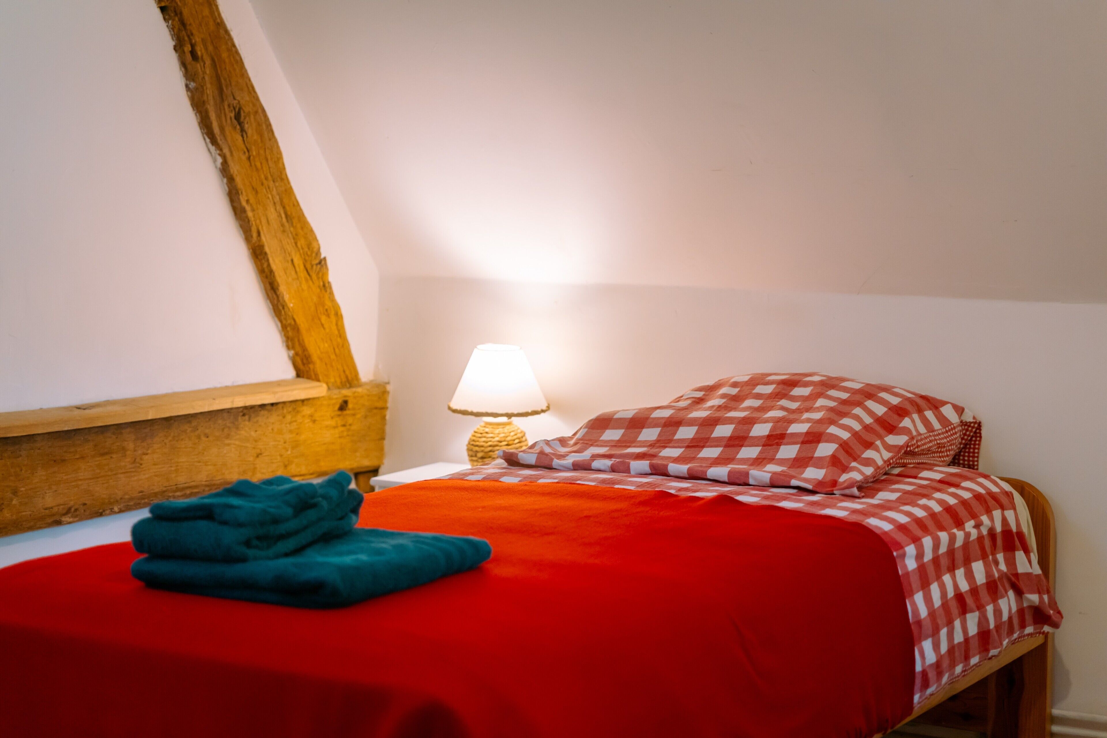 Une chambre à coucher avec une tête de lit en bois, une couvre-lit rouge, un coussin à carreaux et une lampe sur une table de chevet.