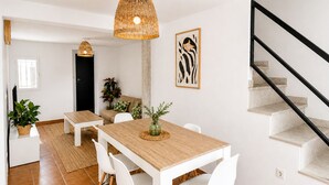A modern dining area with a wooden table, white chairs, a woven pendant light, and a staircase.