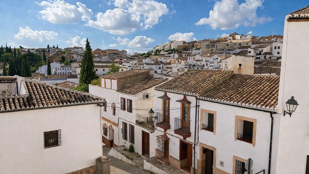 A white building with a tiled roof, a stone-paved courtyard, and a view of a town with similar architecture.