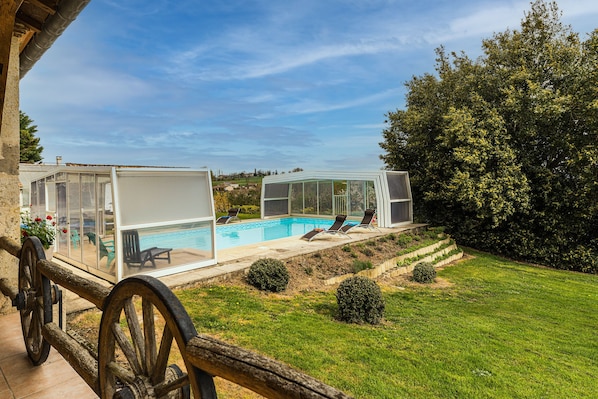 Ein Poolbereich mit Glasveranda, einer Rasenfläche und Blick auf die Landschaft.