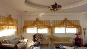 A living room with a sofa, armchair, ottoman, and a coffee table. - Royal Beach Hotel (Karpathos)