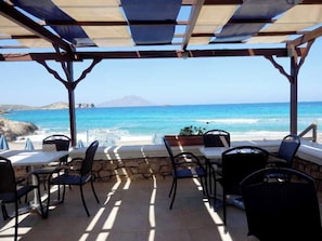 An outdoor seating area with tables and chairs, overlooking a beach and ocean.
