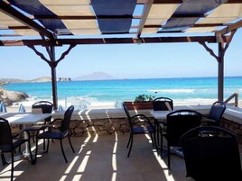Un espacio al aire libre con mesas y sillas, con vista a una playa y el océano.