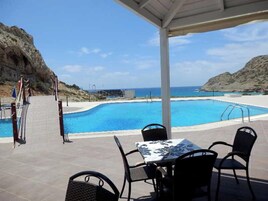 Zona de piscina con mesa y sillas, un espacio de descanso cubierto y vistas al mar.