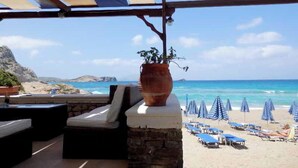 A beachside lounge with outdoor seating, a potted plant, and umbrellas. - Royal Beach Hotel (Karpathos)