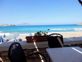 Un área de estar frente a la playa con mesas y sillas, con vista al mar.