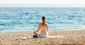 A person meditating on a pebble beach with a view of the sea. - Heritage Hotel Kastelet (Tucepi)
