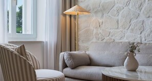 A room with a sofa, a chair, a lamp, and a vase with flowers on a table. - Heritage Hotel Kastelet (Tucepi)