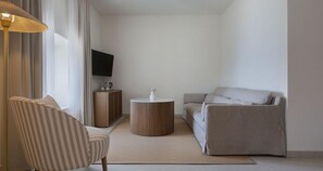 A modern living room with a striped armchair, a round side table, a sofa, a flat-screen TV, and a wooden cabinet. - Heritage Hotel Kastelet (Tucepi)