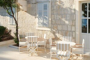 A stone building with a patio area featuring white striped chairs and a round table. - Heritage Hotel Kastelet (Tucepi)