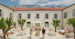 A courtyard with outdoor seating, a central fountain, and a mountain backdrop. - Heritage Hotel Kastelet (Tucepi)