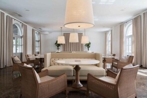 A hotel room with a round dining table, beige sofa, wicker chairs, and a large hanging light fixture. - Heritage Hotel Kastelet (Tucepi)
