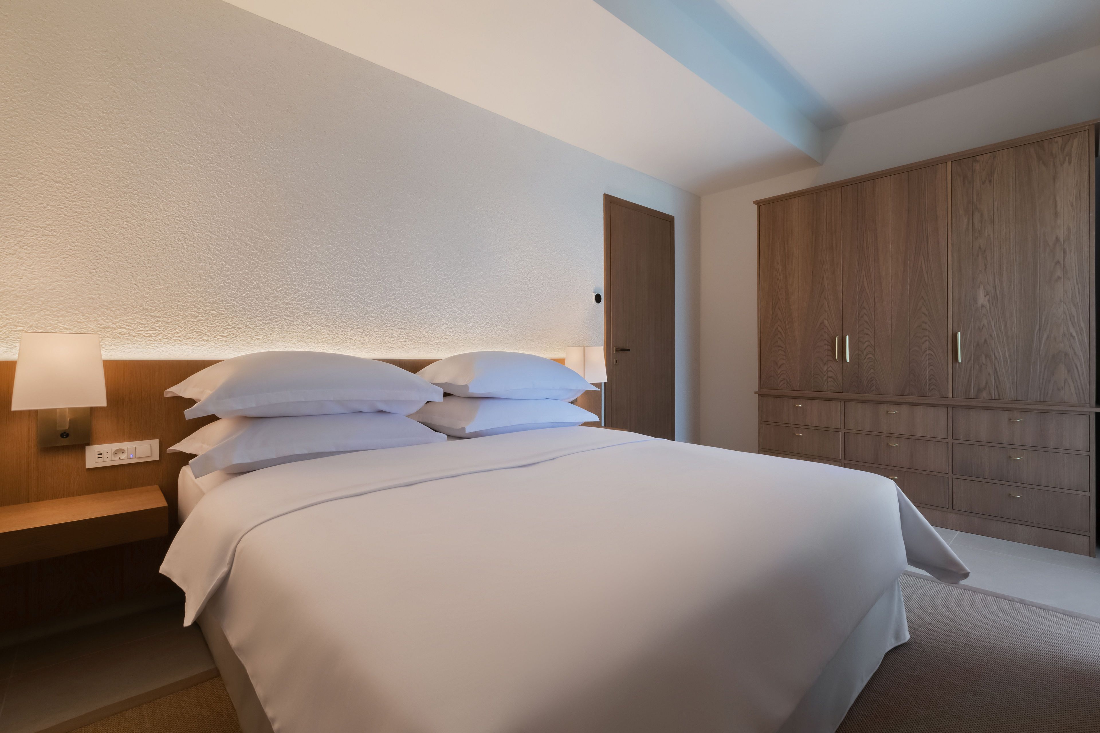 A hotel room with a neatly made bed, a bedside table with a lamp, and a large wardrobe.