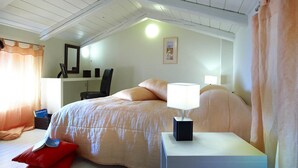 Ein Schlafzimmer mit einem Bett, einem Nachttisch mit Lampe, einem Sessel, einem Schreibtisch mit Spiegel und einem Fenster mit Vorhängen.