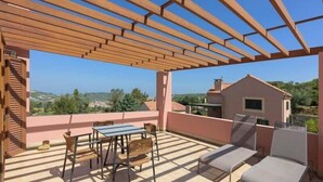 Eine Außenpatio mit einer Holz-Pergola, einem Tisch mit Stühlen und einer Lounge-Ecke mit Kissen.