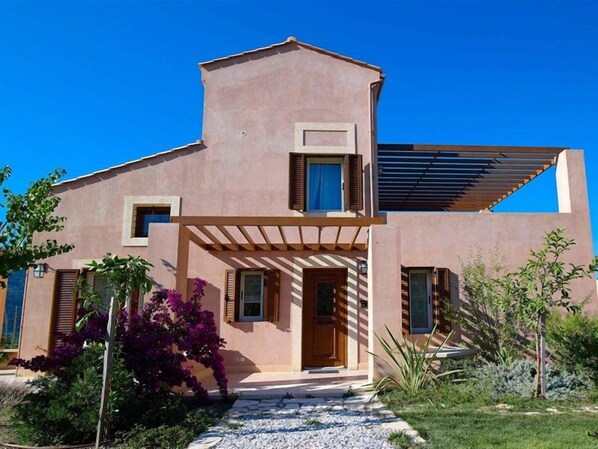 Une maison moderne à deux étages, dotée d’un toit plat, d’une entrée abritée et d’un petit jardin agrémenté de fleurs violettes.