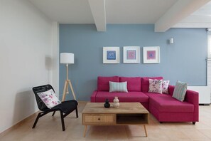 Una sala de estar con un sofá rosa, una silla negra, una mesa de centro de madera y tres obras de arte enmarcadas en la pared.