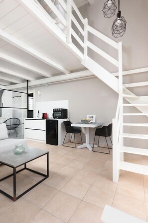 A modern kitchen with white cabinetry, a black refrigerator, and a dining area with a white table and chairs. - Eliathos Residence Houses Archanes (Archanes-Asterousia)
