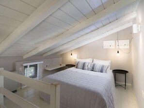 Une chambre avec un plafond en pente, un lit recouvert d’une couette blanche, deux tables de chevet et des lampes fixées au mur.