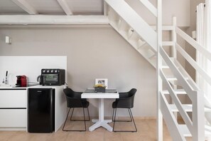 A compact kitchen with a white countertop, a black refrigerator, a red coffee machine, and a small table with two black chairs. - Eliathos Residence Houses Archanes (Archanes-Asterousia)