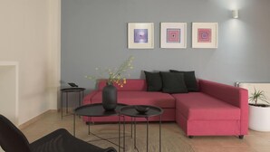Uma sala de estar moderna com um sofá vermelho, duas mesas de centro pretas e um vaso com flores. Há três obras de arte emolduradas na parede.