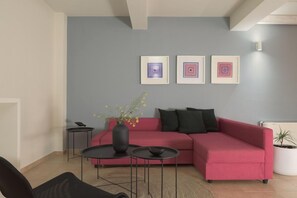 Una sala de estar moderna con un sofá rojo, dos mesas de centro negras y un jarrón con flores. Hay tres cuadros enmarcados en la pared.