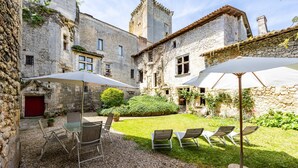 A courtyard with stone buildings, a red door, and outdoor seating with umbrellas.
