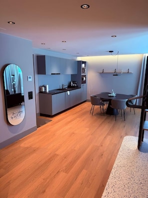 A modern kitchen with a dining area, wooden flooring, and a large mirror. - Aparthotel Goldey (Unterseen)