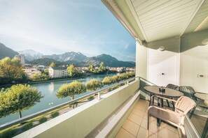 A balcony with a view of a river and mountains, a table, and two chairs. - Aparthotel Goldey (Unterseen)
