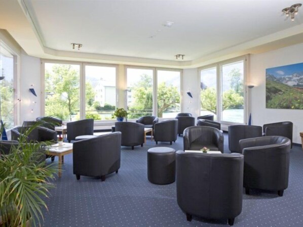 A hotel lobby with multiple seating areas, large windows, and a view of greenery outside. - Aparthotel Goldey (Unterseen)
