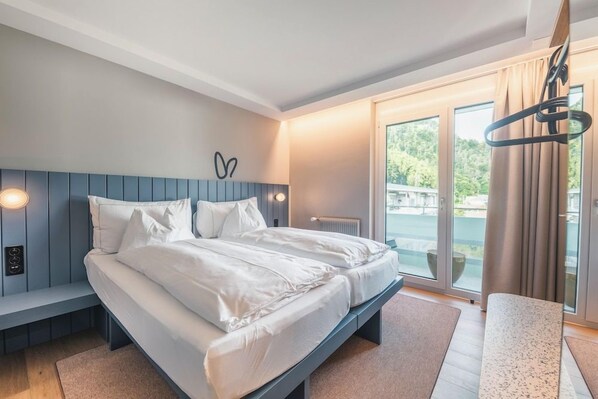 A modern bedroom with a large bed, a bench, and a view of the outdoors. - Aparthotel Goldey (Unterseen)