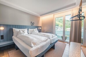 A modern bedroom with a large bed, a bench, and a view of the outdoors. - Aparthotel Goldey (Unterseen)