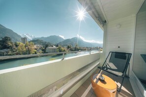 A balcony with a view of a river and mountains, a chair, and a small table. - Aparthotel Goldey (Unterseen)