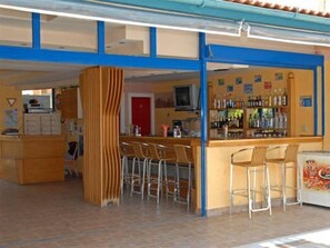 Una zona de bar con taburetes, una barra llena de botellas y un televisor.