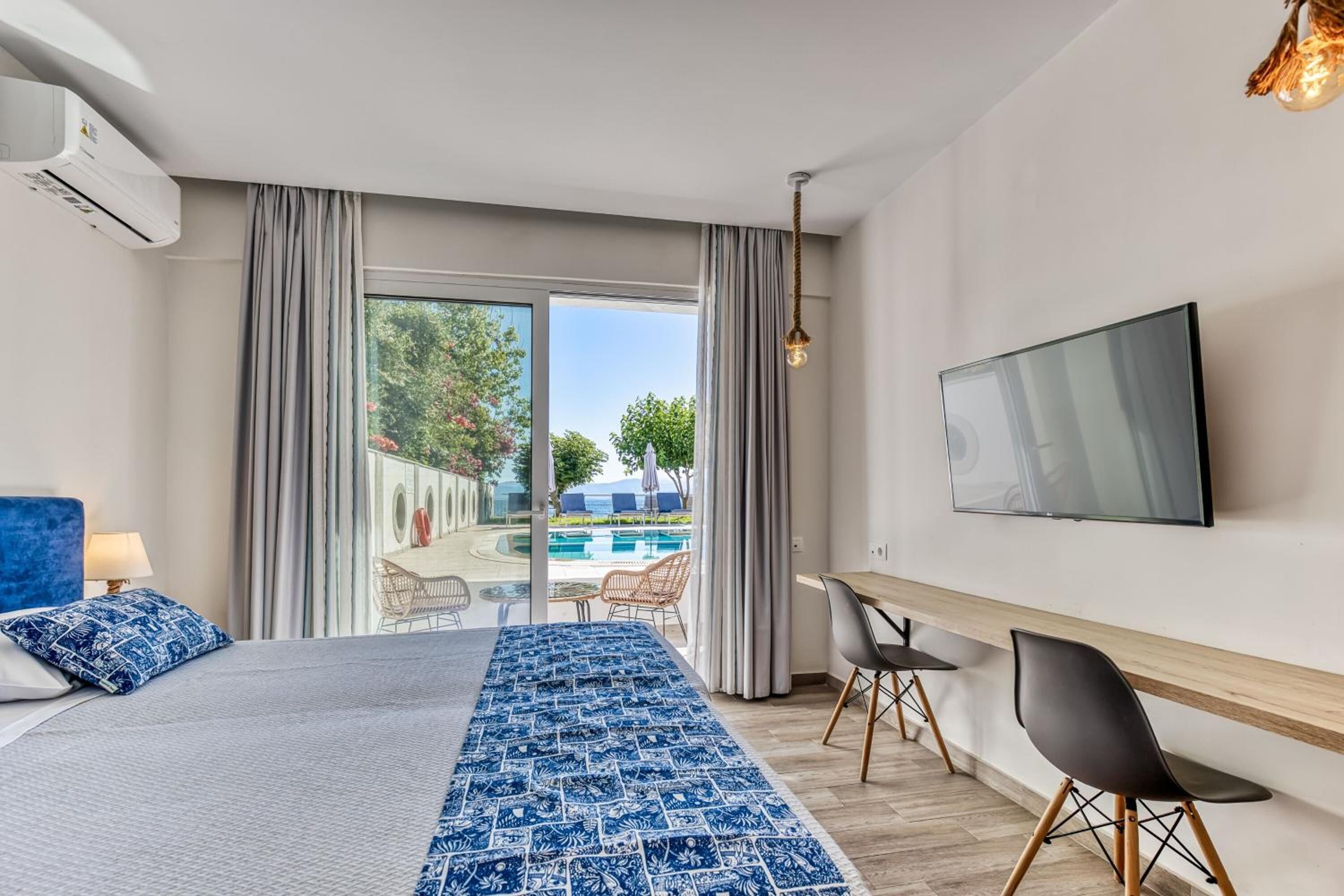 Ein Hotelzimmer mit Bett, Fernseher, Schreibtisch und Blick auf einen Außenpool.