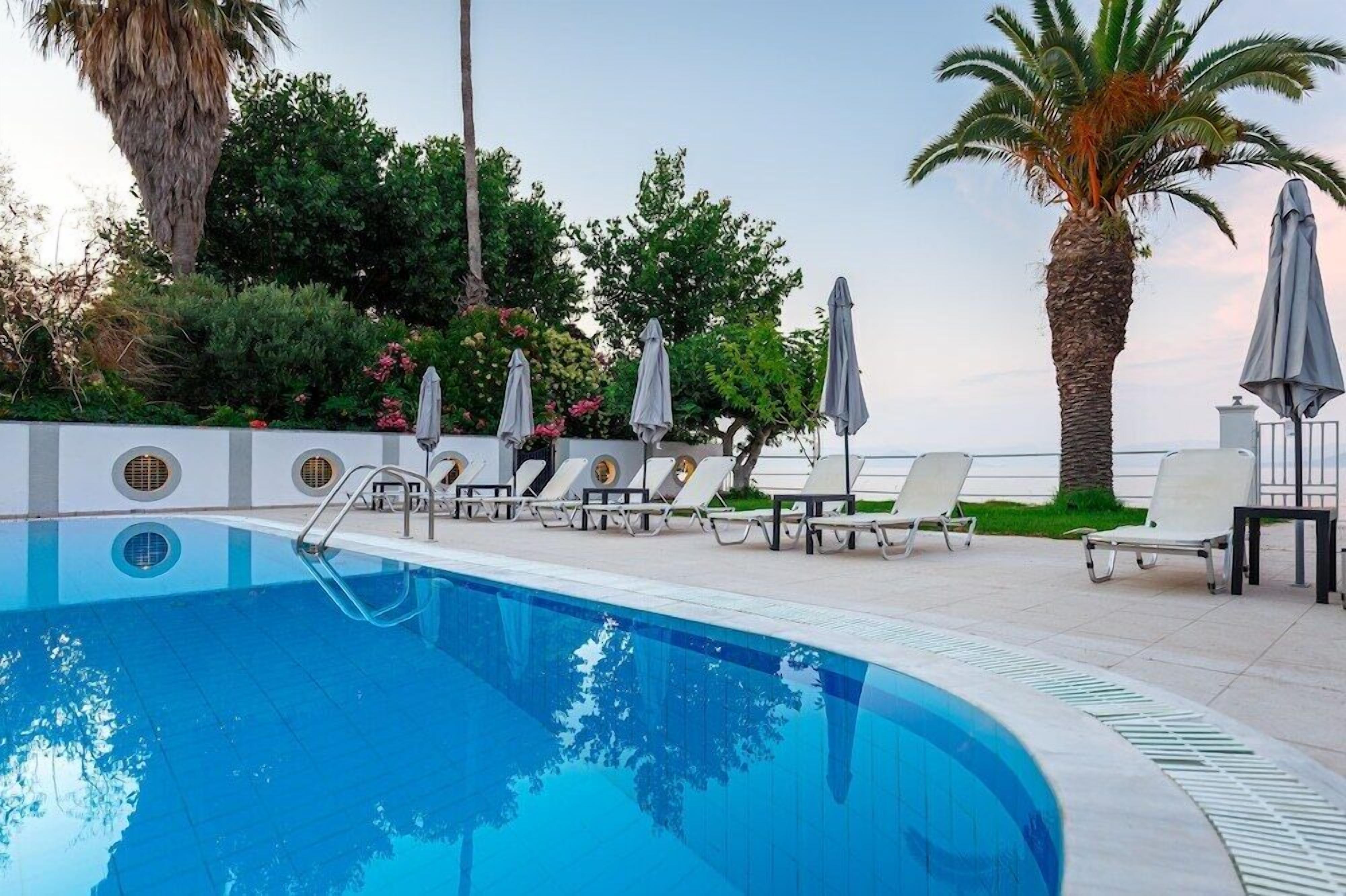 Ein Swimmingpool mit Liegestühlen und Sonnenschirmen, umgeben von Palmen und viel Grün.