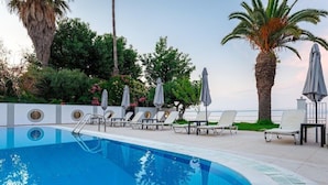 A swimming pool with lounge chairs and umbrellas, surrounded by palm trees and greenery. - Sirocco Hotel (Corfu)