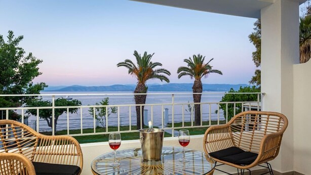 A balcony with wicker chairs, a glass table, and a view of the sea. - Sirocco Hotel (Corfu)