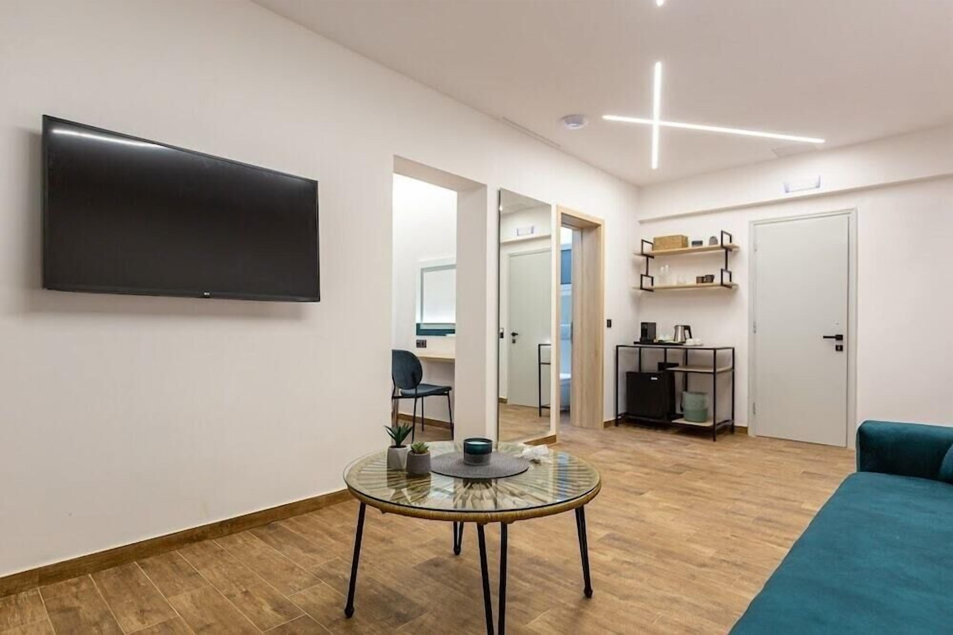 Ein modernes Wohnzimmer mit Flachbildfernseher, Glastisch, Sofa und einer Küche im Hintergrund.