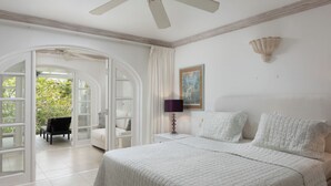 A bedroom with a bed, two bedside tables, a chair, and a door leading to a balcony. - Royal Westmoreland Cassia Heights 29 - by Zenbreak (Westmoreland)