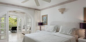 A bedroom with a bed, two nightstands, a lamp, a painting, and a view through an arched doorway to an outdoor seating area.
