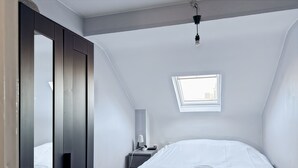 Una camera da letto con un letto, un comodino, una lampada, una finestra e un armadio.