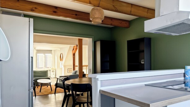 Una cucina moderna con soffitto in legno, zona pranzo con tavolo e sedie, e vista su un'altra stanza.