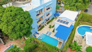 Ein mehrstöckiges Hotel mit Pool auf dem Dach, einem separaten Schwimmbecken und einem üppigen, grünen Garten.