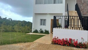 A modern two-story building with a stone facade, a staircase with black railings, and a small garden with red flowers. - Beautiful and Cozy With sea Views (Las Terrenas)